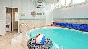 Una piscina interior con un flotador azul inflable, una escalera de metal y una pared de azulejos con un adorno.