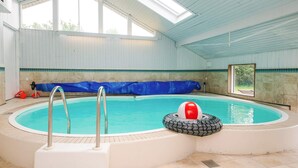 Una piscina interior con vista despejada del cielo gracias a tragaluces, una escalera de piscina y una pelota roja y blanca flotando.