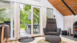 Ein modernes Interieur mit Holzboden, einem grauen Sessel, einem Kamin und einer Schiebeglastür, die auf eine Außenpatio führt.