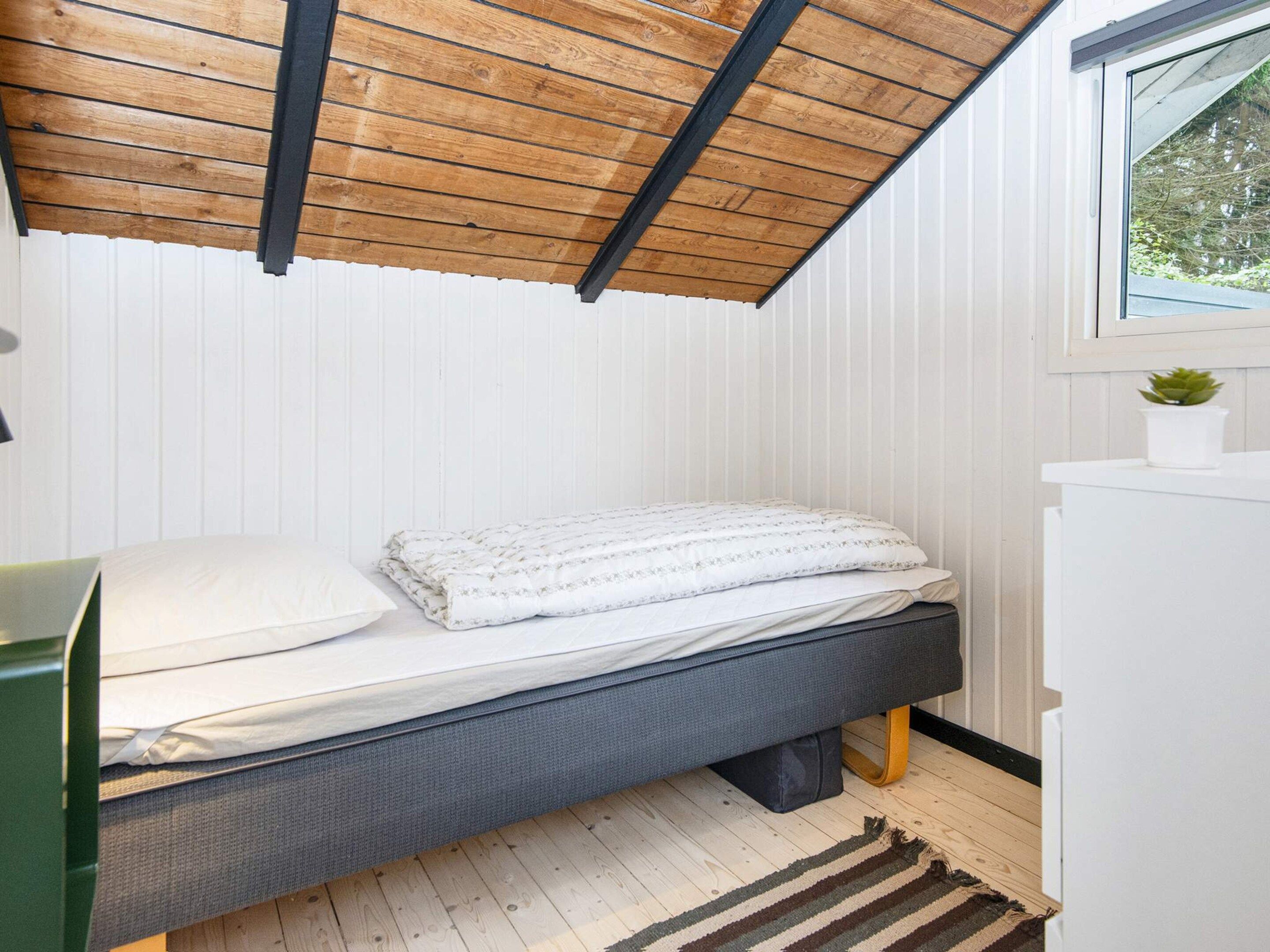 Un dormitorio compacto con una cama individual, un escritorio pequeño y una ventana con vistas a zonas verdes.