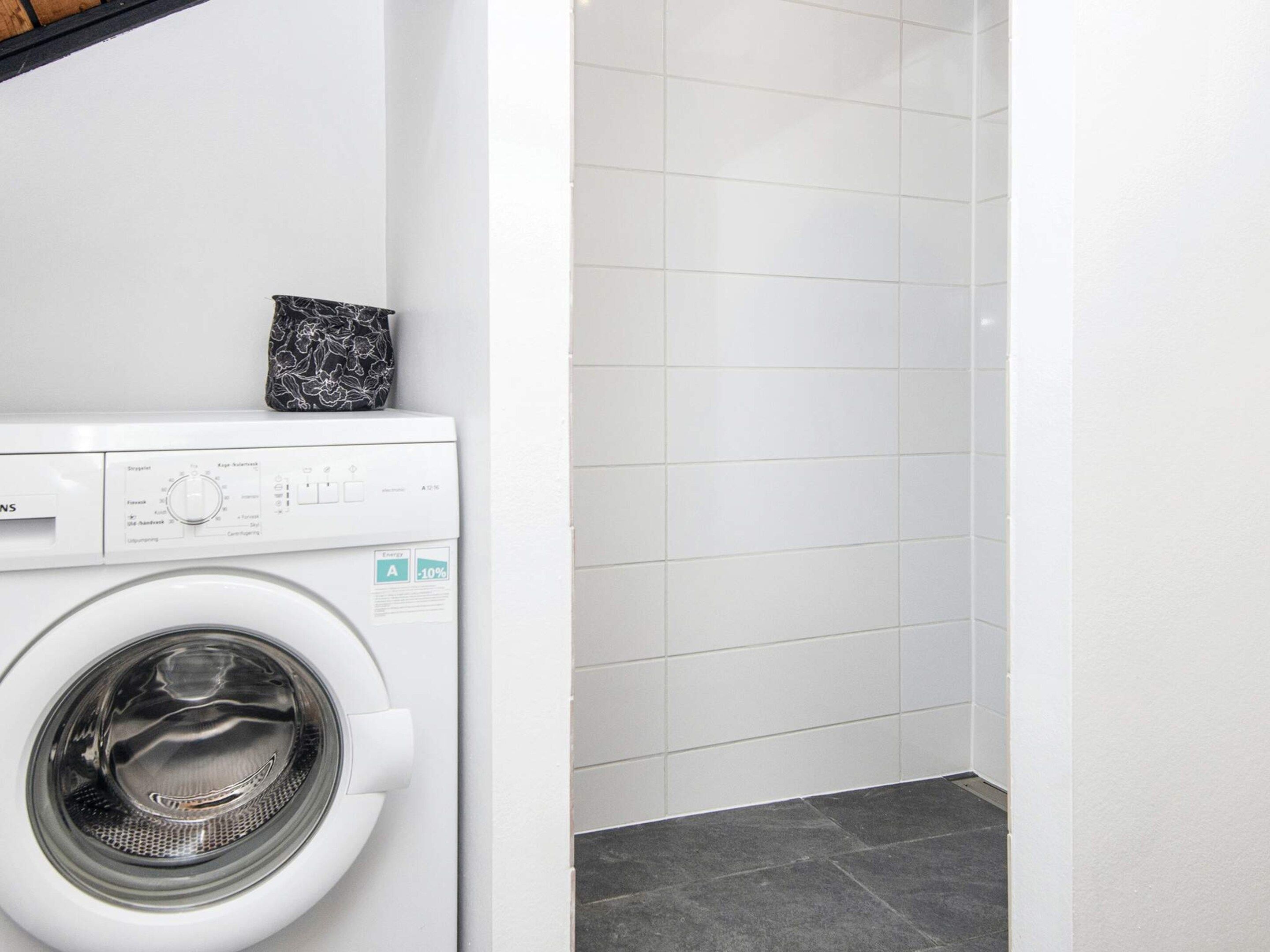 A compact laundry room with a front-loading washing machine and a tiled wall.