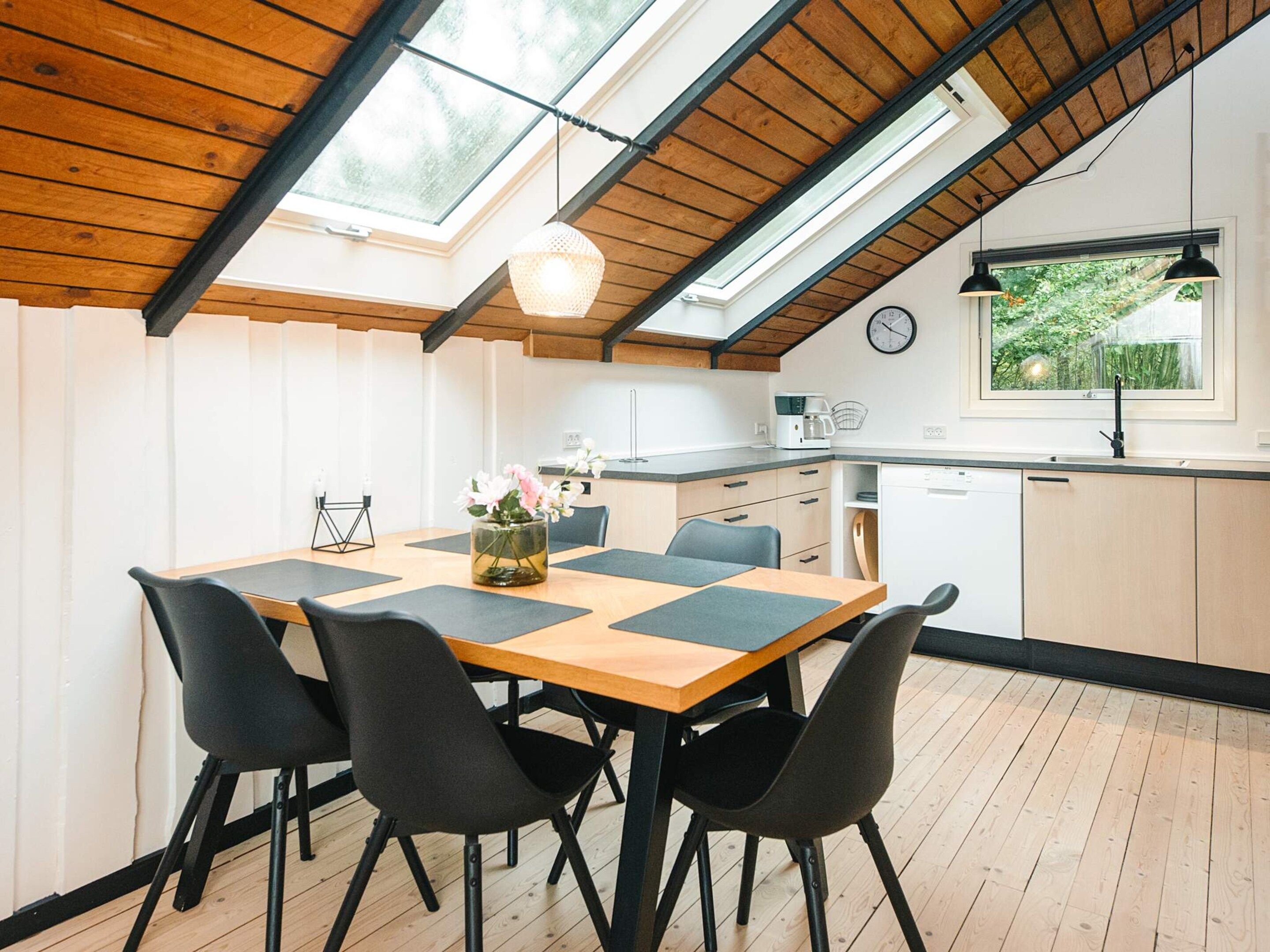 A dining area with a wooden table, black chairs, and a vase of flowers.
