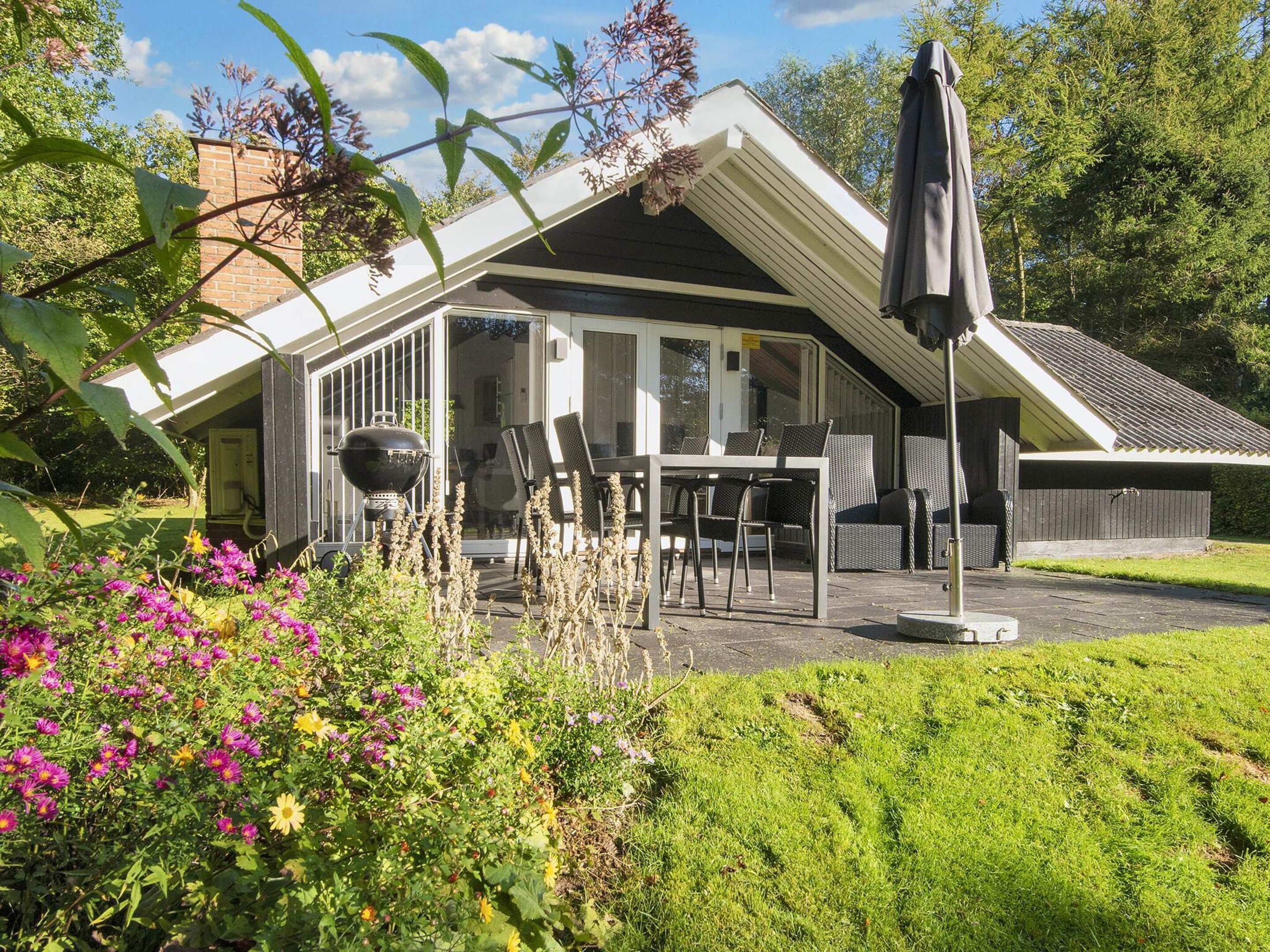A covered outdoor seating area with a table and chairs, a grill, and a patio umbrella.