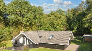 Ein eingeschossiges Haus mit geneigtem Dach, einer kleinen Veranda und einer Terrassenfläche.