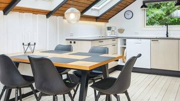 Una cocina moderna con comedor, que presenta una mesa de madera, sillas negras, una lámpara colgante y un reloj en la pared.