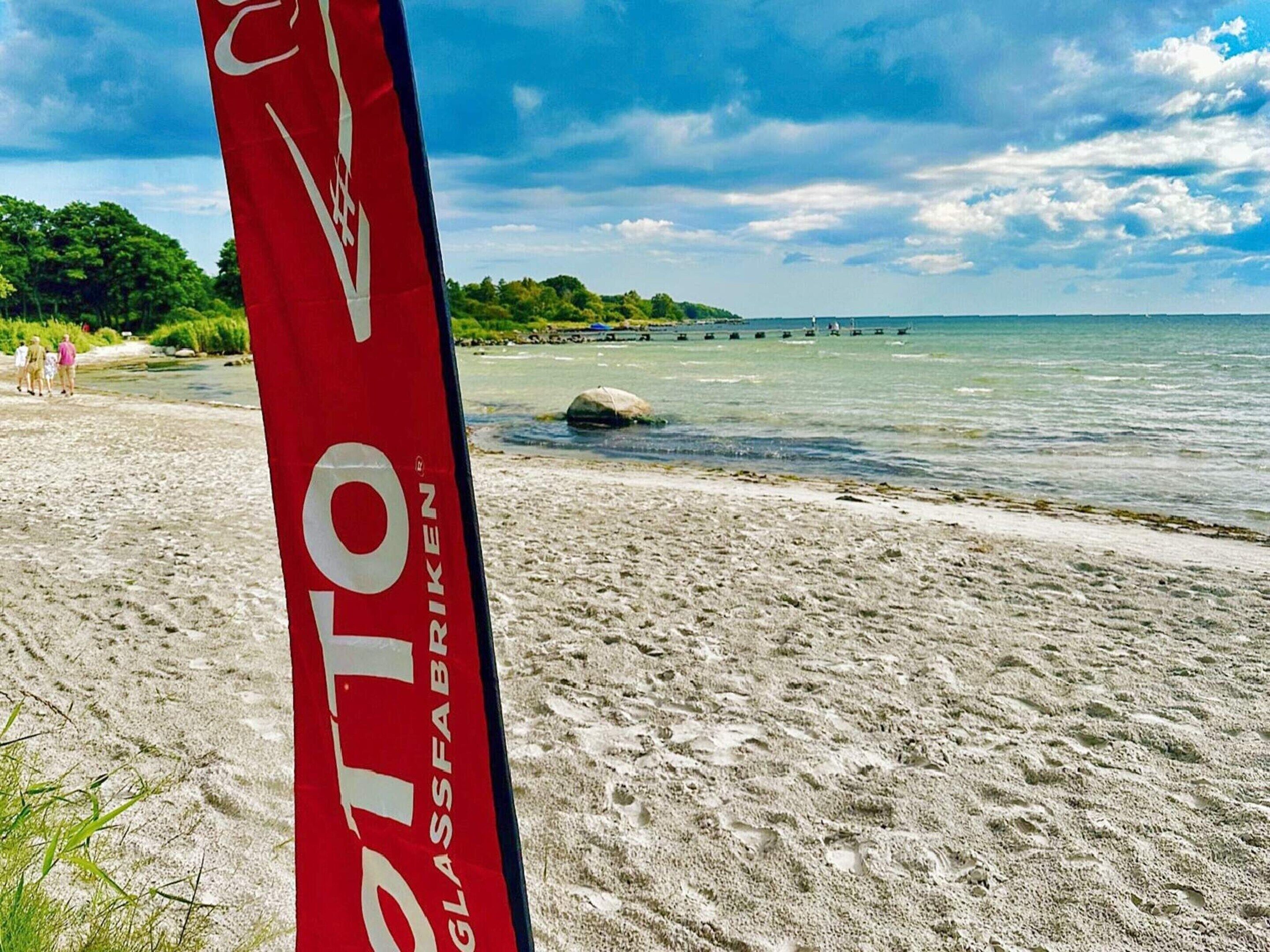 A beach with a red banner reading "OTTO GLASSFABRIKEN".