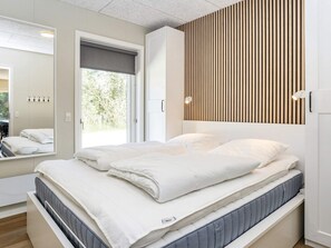 A modern bedroom with a bed, a large mirror, a window with a view of greenery, and a wooden slat wall design. - 5 Star Holiday Home in Oster Assels (Øster Assels)