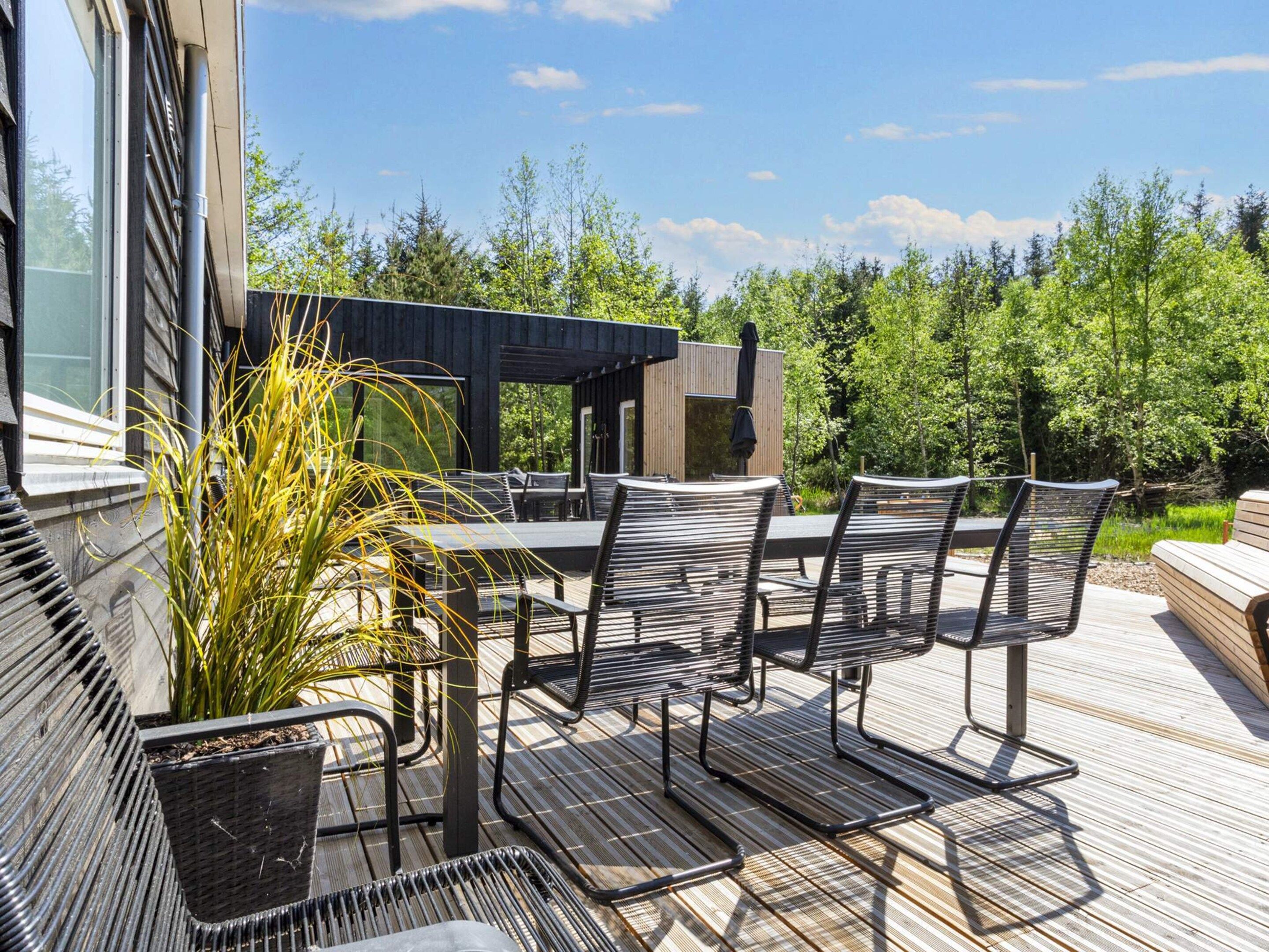 Een terras buiten, met een tafel en stoelen, omringd door begroeiing en een houten terras.