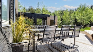 An outdoor patio with a table and chairs, surrounded by greenery and a wooden deck. - 5 Star Holiday Home in Oster Assels (Øster Assels)