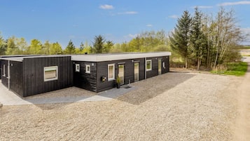 A modern, single-story building with a gravel driveway and a forested background.