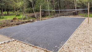 A volleyball court with a net, surrounded by trees and wood chips. - 5 Star Holiday Home in Oster Assels (Øster Assels)
