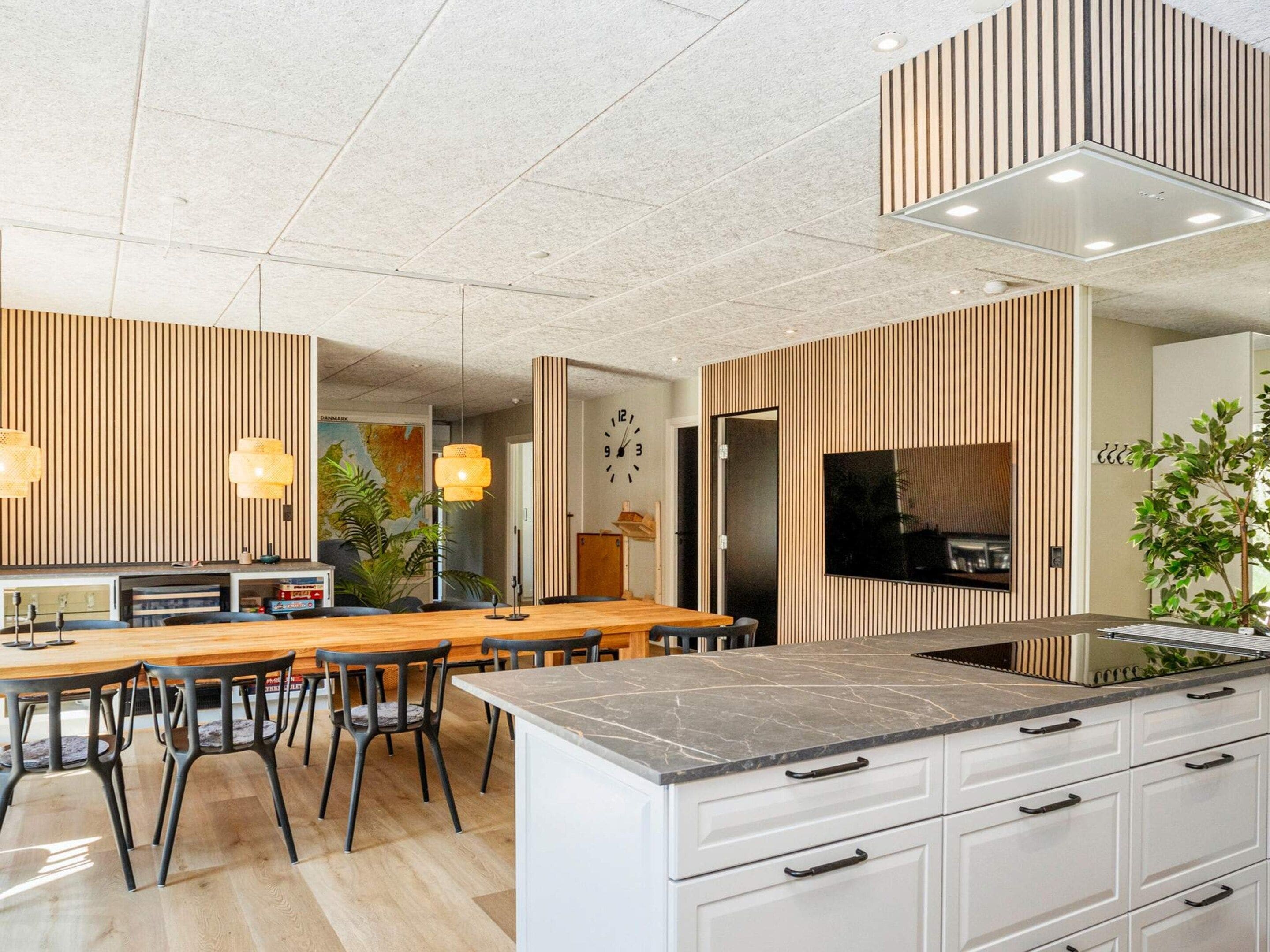 Une cuisine moderne dotée d’un îlot central, de meubles blancs et d’un grand téléviseur à écran plat fixé au mur.