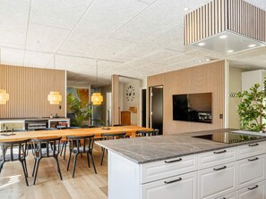 A modern kitchen with a central island, white cabinetry, and a large flat-screen TV mounted on the wall. - 5 Star Holiday Home in Oster Assels (Øster Assels)