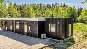 A modern, single-story building with a gravel driveway and a forested backdrop. - 5 Star Holiday Home in Oster Assels (Øster Assels)