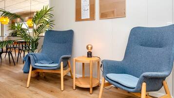 Een zithoek met twee blauwe fauteuils, een klein houten tafeltje met een lamp, en een prikbord aan de muur.