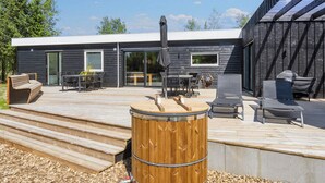A modern outdoor deck with a barbecue grill, seating area, and a wooden barrel. - 5 Star Holiday Home in Oster Assels (Øster Assels)