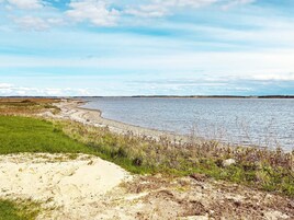 A coastal landscape with a sandy beach, grassy areas, and a calm body of water.