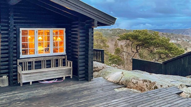 A log cabin with a satellite dish, a wooden deck, and a window with warm interior lighting. - 10 Person Holiday Home in Skjaerhalden (Hvaler)