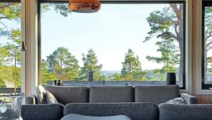 A modern living room with a grey sofa, a table with a glass vase, and a view of trees and hills.