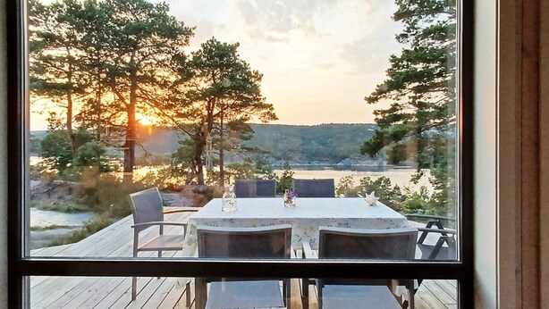 A wooden deck with a table and chairs overlooking a lake at sunset.