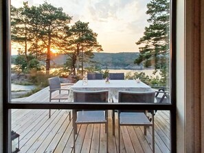 A wooden deck with a table and chairs overlooking a lake at sunset. - 4 Star Holiday Home in Risor (Risør)