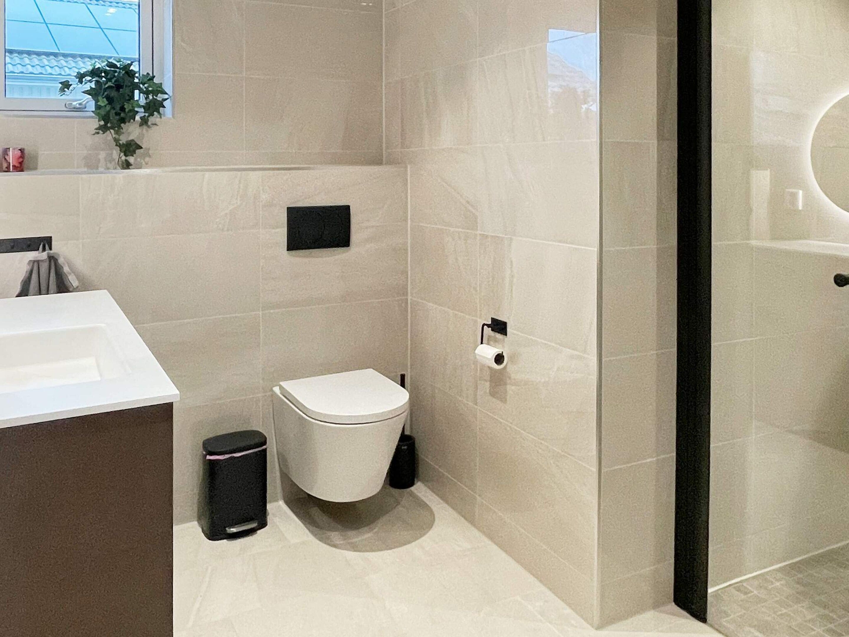 A modern bathroom with a toilet, sink, and trash bin.