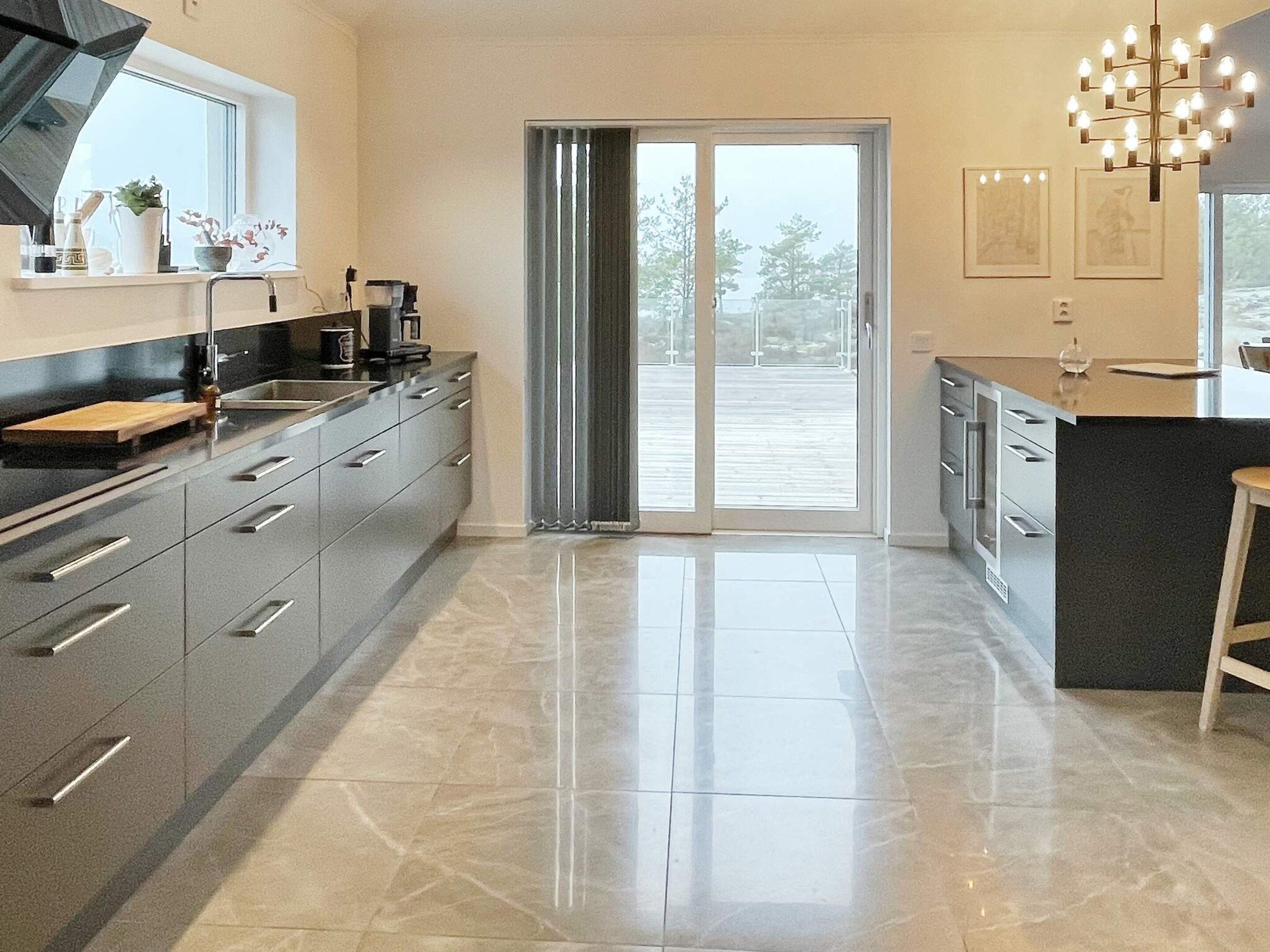 A modern kitchen with a large island, sliding glass doors leading to an outdoor area, and a chandelier.