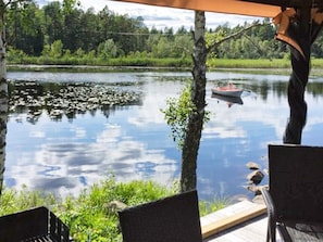 En træterrasse ved søen med stole og en båd på vandet.