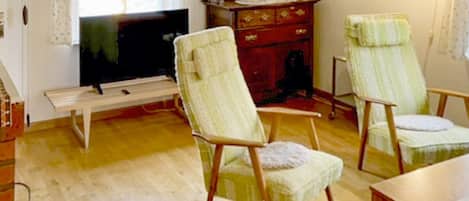 Un salon comprenant un téléviseur, deux fauteuils, une table en bois et un tapis à motifs.