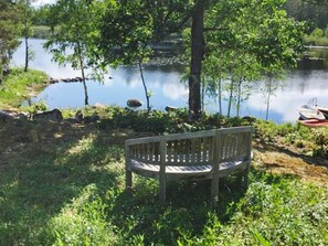 A wooden bench by a lake with a boat docked in the background. - 4 Person Holiday Home in Rockneby (Rockneby)