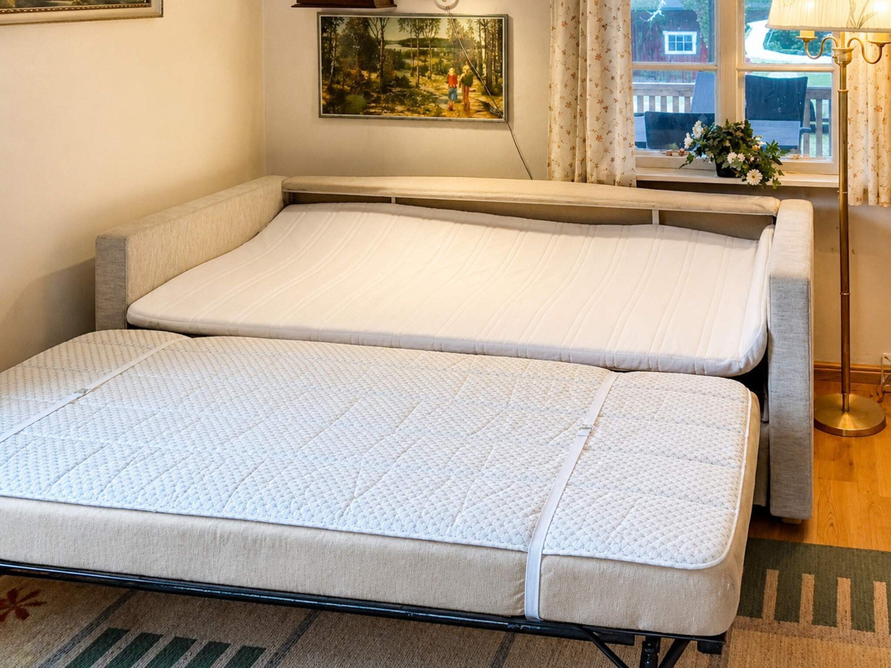A room with two beds, a window with curtains, a painting on the wall, and a floor lamp.