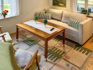 Una sala de estar con un sofá, una mesa de centro de madera, un tapete estampado y una ventana con cortinas.
