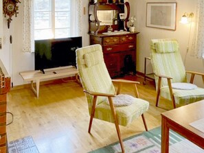 Una sala de estar con piso de madera, un televisor, un mueble de madera y dos sillones tapizados.