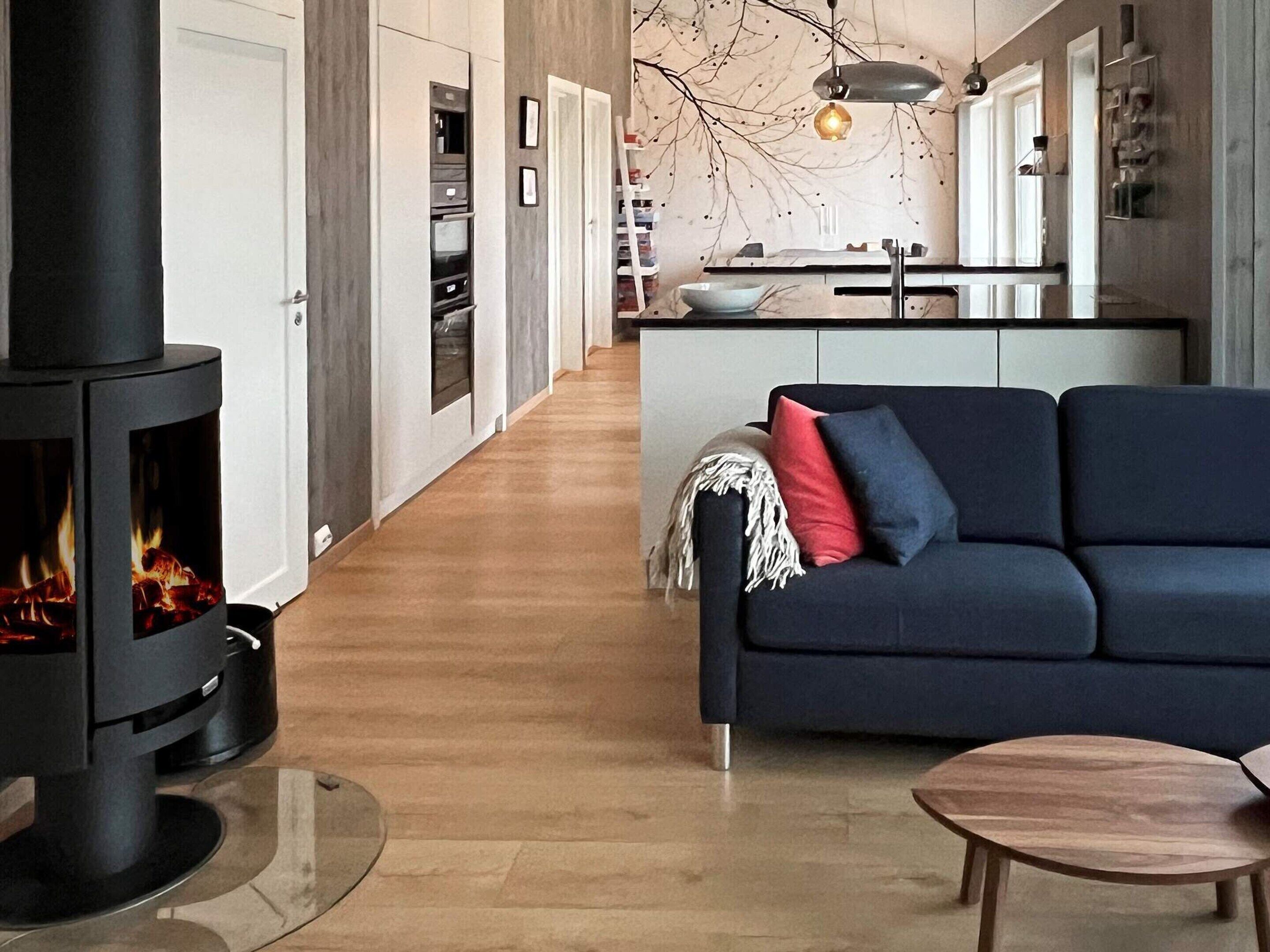 Un salon moderne avec un poêle à bois noir, un canapé bleu foncé et une table basse en bois.