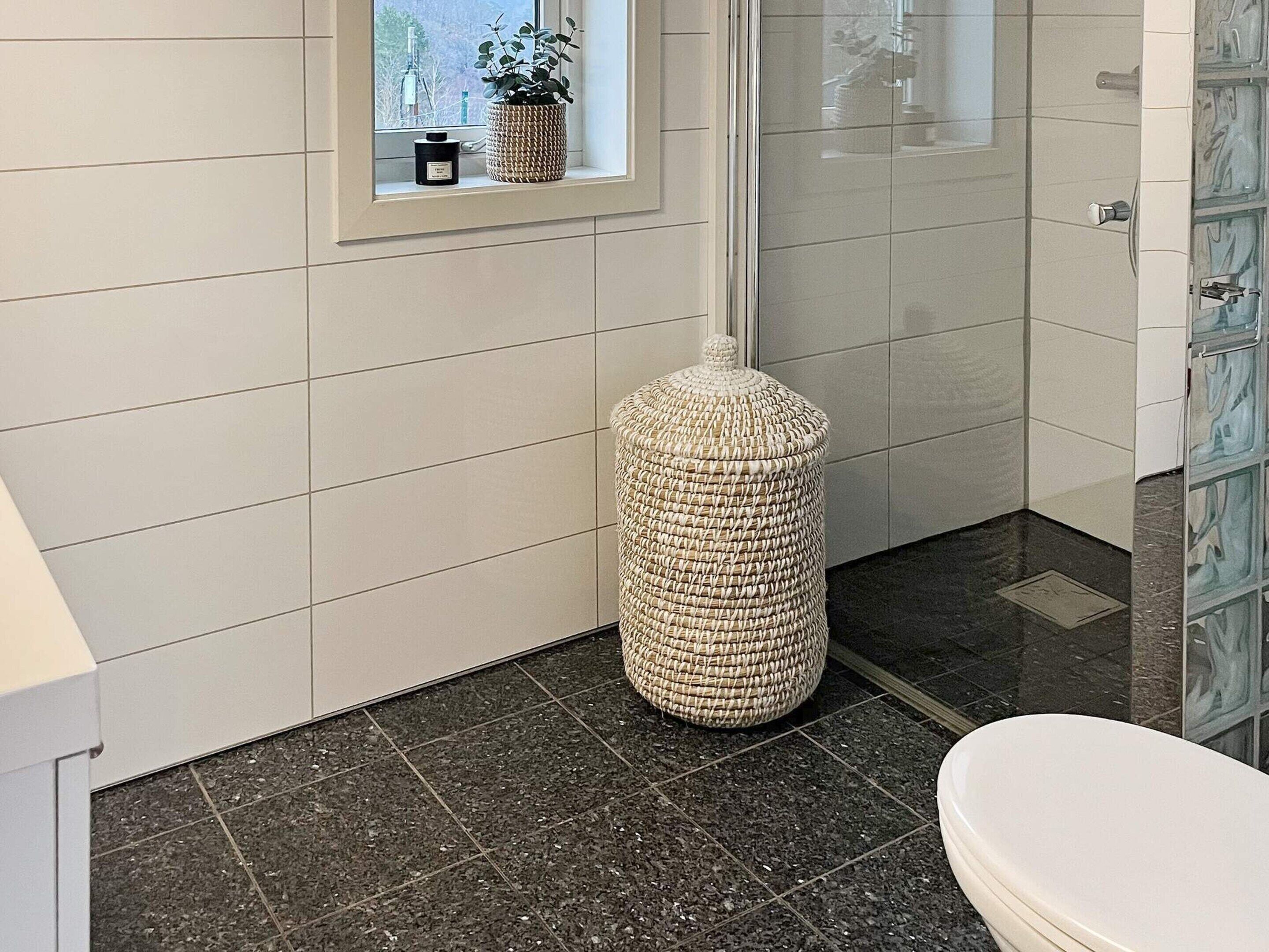 A bathroom with a toilet, a woven basket, and a window with plants.