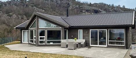 A modern house with large windows, a patio, and a mountainous backdrop.