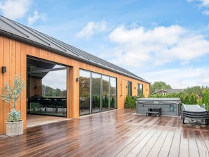 Un bâtiment moderne en bois, doté de grandes portes vitrées, d’une terrasse et de mobilier d’extérieur.