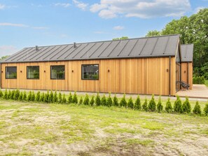 A modern wooden building with a metal roof, multiple windows, and a paved entrance area. - 5 Star Holiday Home in Ansager (Ansager)