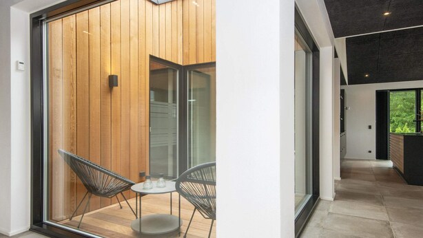 A modern interior with a sliding glass door leading to an outdoor area, featuring a wooden wall, two black chairs, and a small table. - 5 Star Holiday Home in Ansager (Ansager)