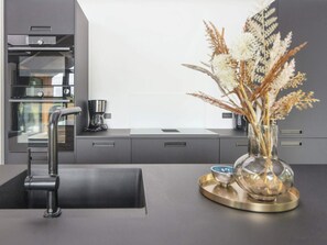 A modern kitchen with a built-in oven, a coffee maker, and a vase with dried flowers on the counter. - 5 Star Holiday Home in Ansager (Ansager)
