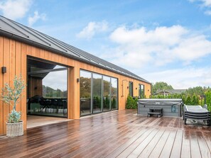 A modern house with a wooden exterior, large sliding glass doors, a deck, and outdoor furniture. - 5 Star Holiday Home in Ansager (Ansager)