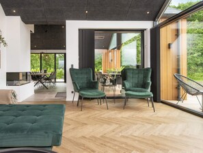 A modern interior with a herringbone floor, a green sofa, and a dining area with a view of greenery. - 5 Star Holiday Home in Ansager (Ansager)
