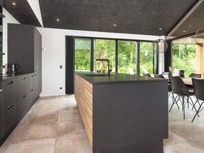 A modern kitchen with a central island, large windows, and a dining area with chairs. - 5 Star Holiday Home in Ansager (Ansager)