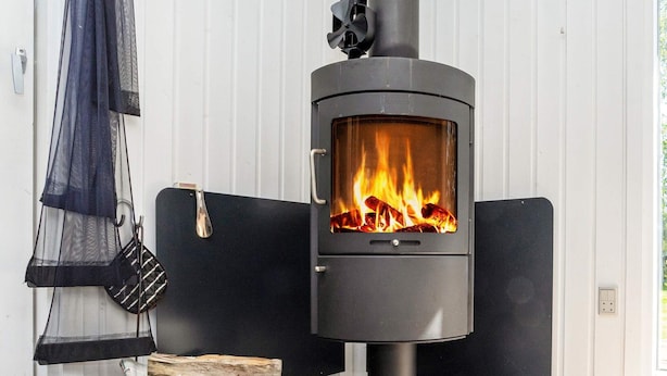 Ein moderner Kaminofen mit Glasscheibe, ein Holzkorb und ein aufgehängter Gegenstand.