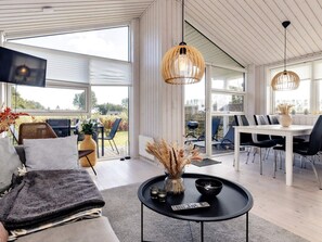 A modern interior with a sofa, a round black table with a remote, and a dining area with chairs and a white table. - 4 Star Holiday Home in Vaeggerlose (Vaeggerlose)