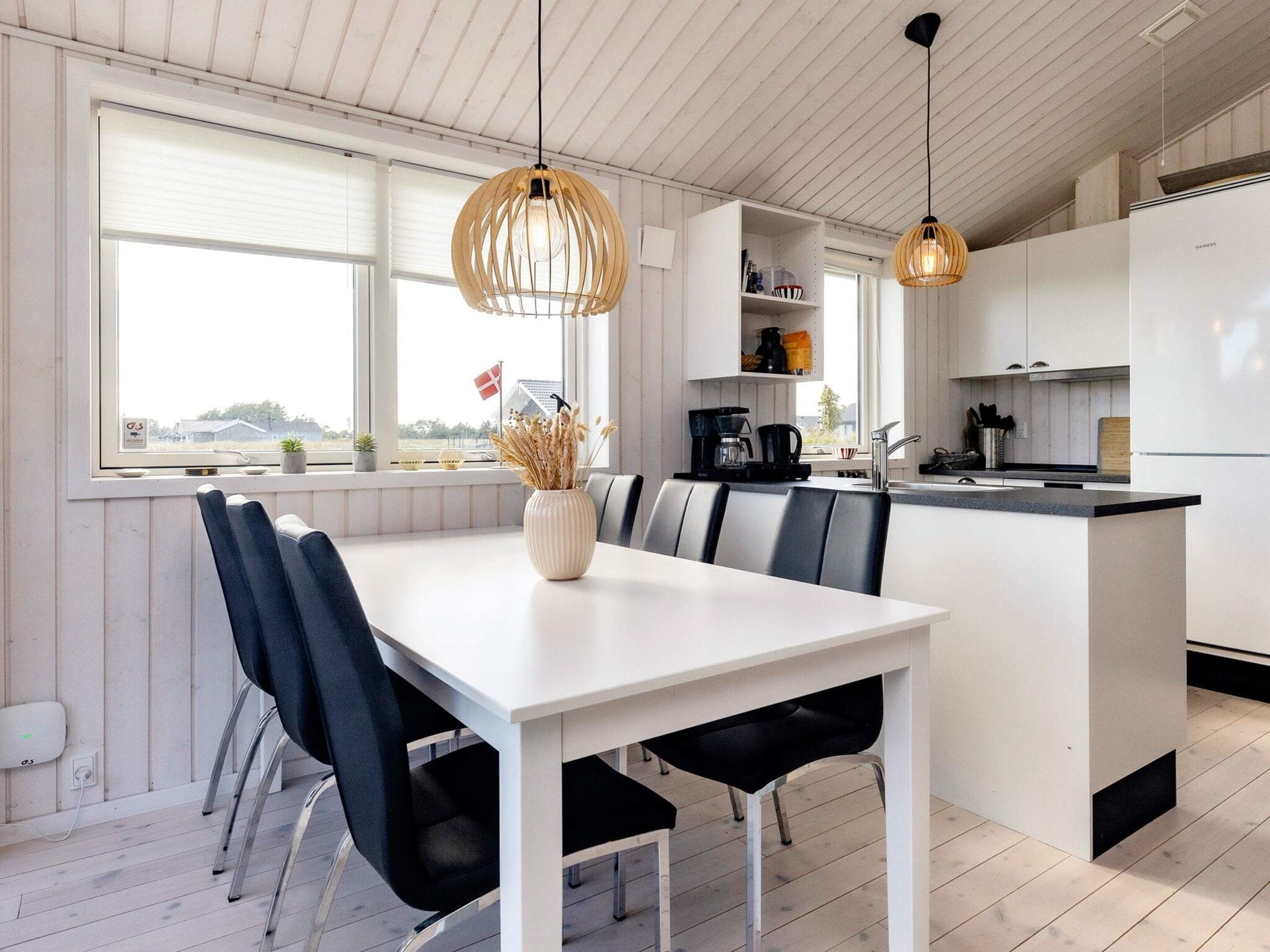 A modern kitchen with a dining area, white cabinetry, and pendant lighting.