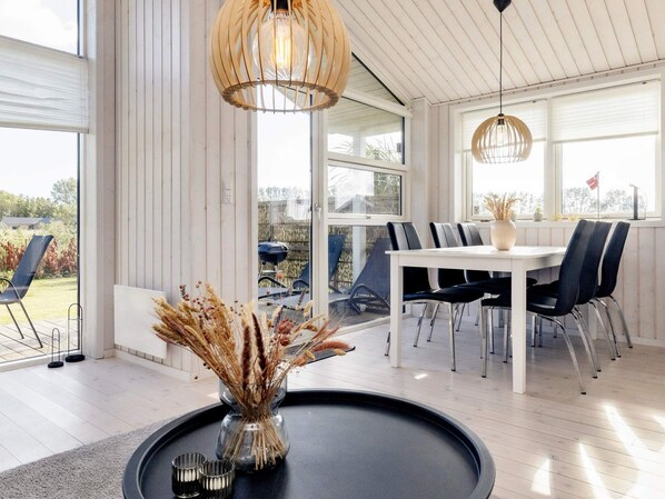 A modern dining area with a white table and black chairs, a vase with dried plants, and a hanging light fixture. - 4 Star Holiday Home in Vaeggerlose (Vaeggerlose)