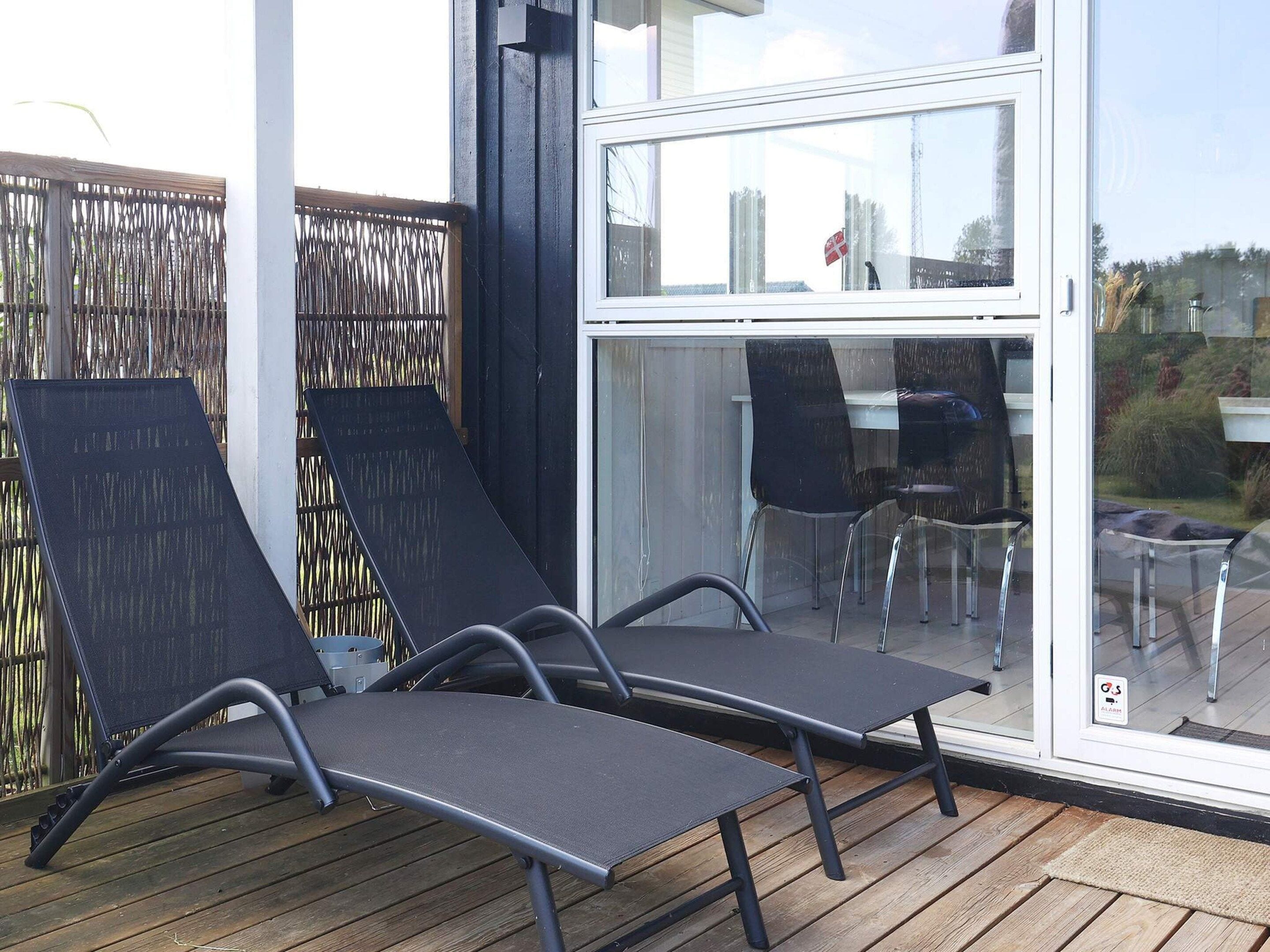 Une terrasse avec deux chaises longues et une table, une porte vitrée donnant sur un espace extérieur et une clôture en bois.