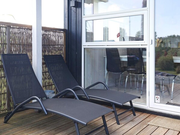 A deck with two lounge chairs and a table, a glass door leading to an outdoor area, and a wooden fence. - 4 Star Holiday Home in Vaeggerlose (Vaeggerlose)