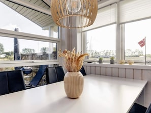 A dining area with a white table, black chairs, a vase with dried plants, and a Danish flag on the windowsill. - 4 Star Holiday Home in Vaeggerlose (Vaeggerlose)